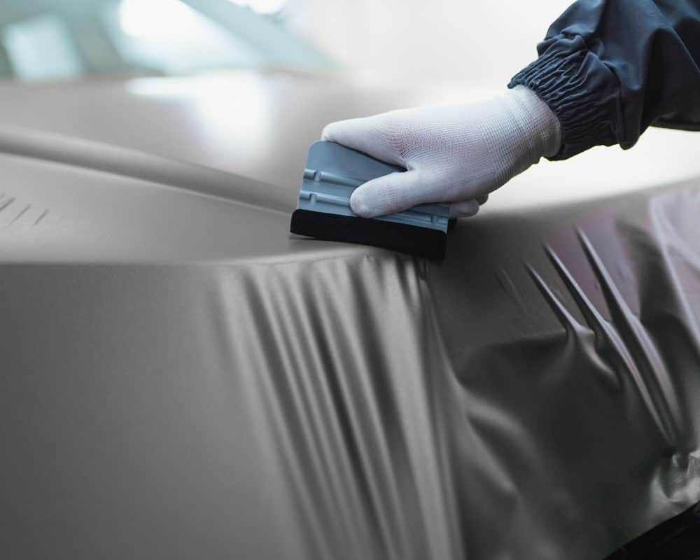 Car Wrap instructor smoothing out film over vehicle's trunk