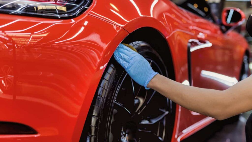 Car detailer using a foam applicator to condition tires on a red Porsche Carrera