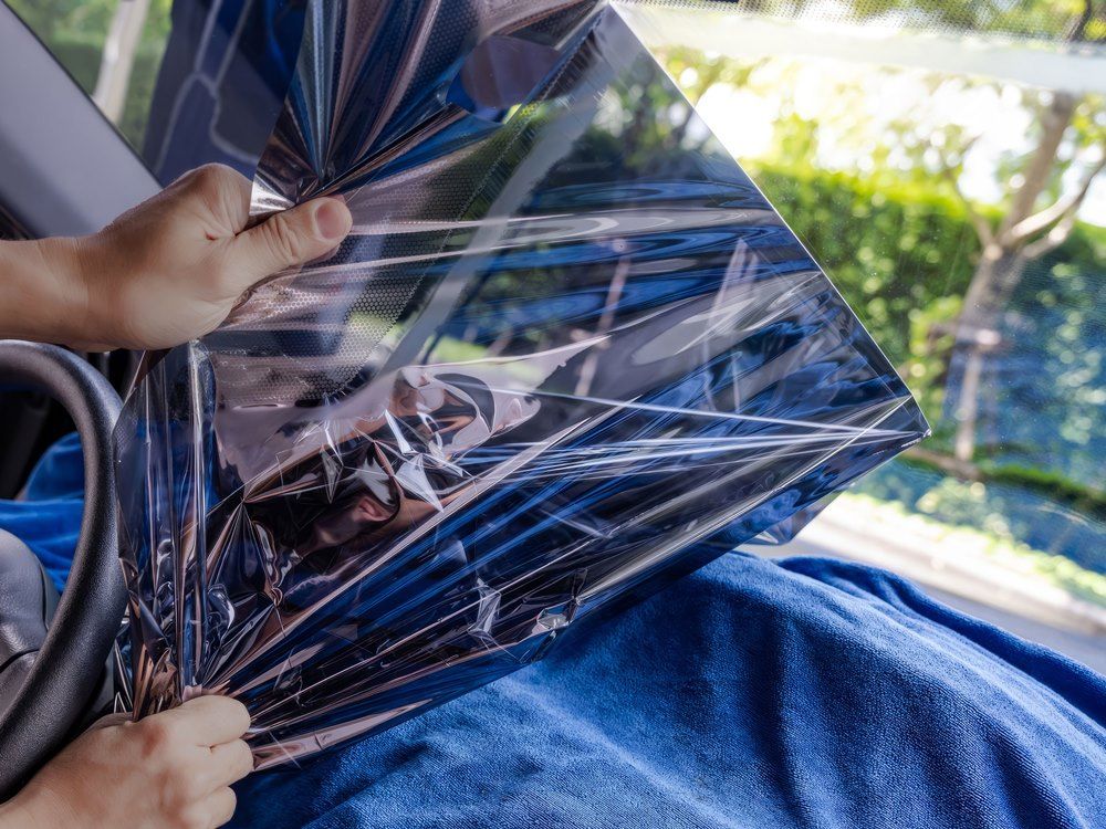 Professional technician meticulously peeling off old tint from a car windshield on a sunny morning.