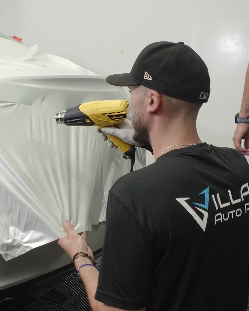 Professional Wrap Specialist meticulously applying vinyl film to a vehicle using a heat gun for a smooth, flawless finish.