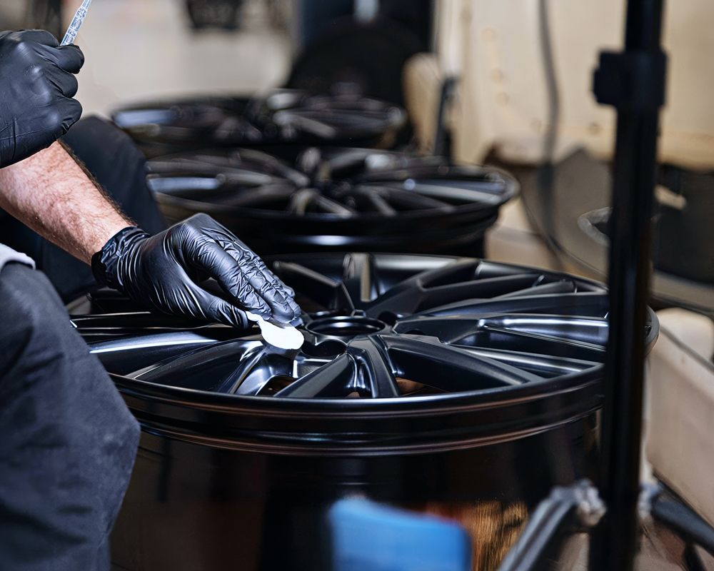 Specialist meticulously applying high-gloss ceramic coating to custom wheels for enhanced durability and shine